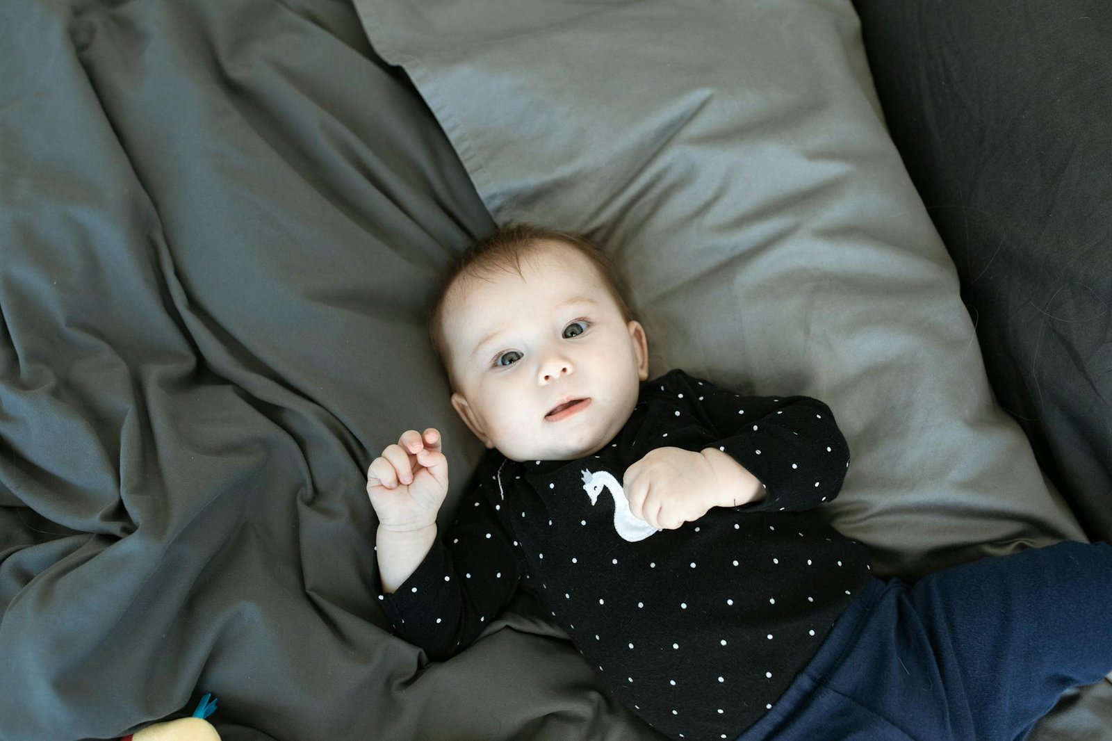 Cute baby in polka dot outfit lying on bed, looking up with curious expression.